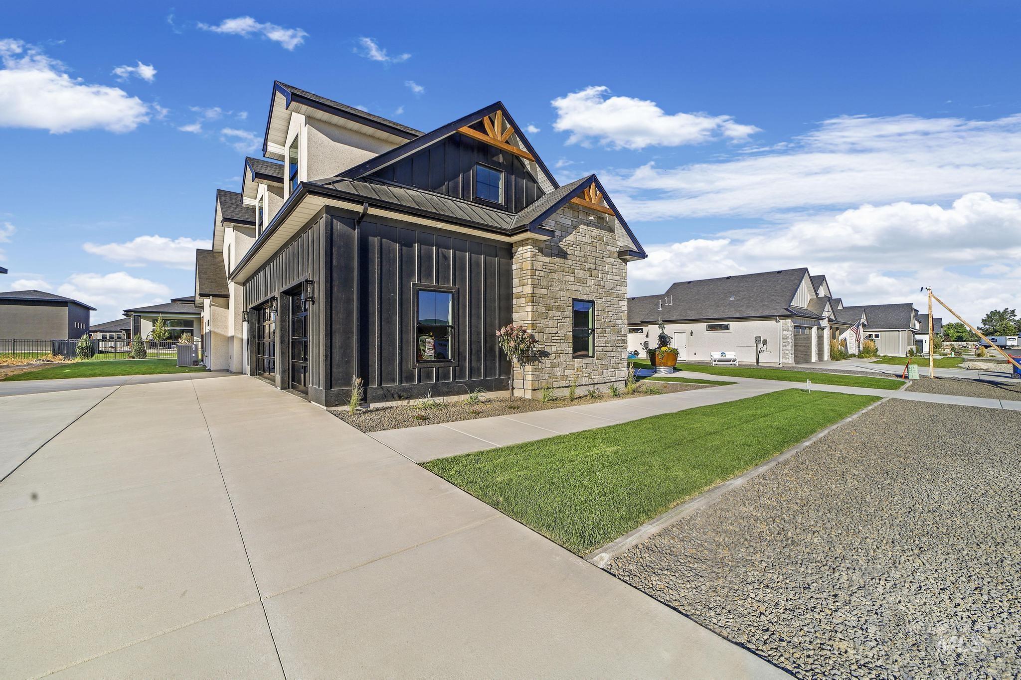 View of front of house with board and batten siding, stone siding, a front yard, a residential view, and concrete driveway