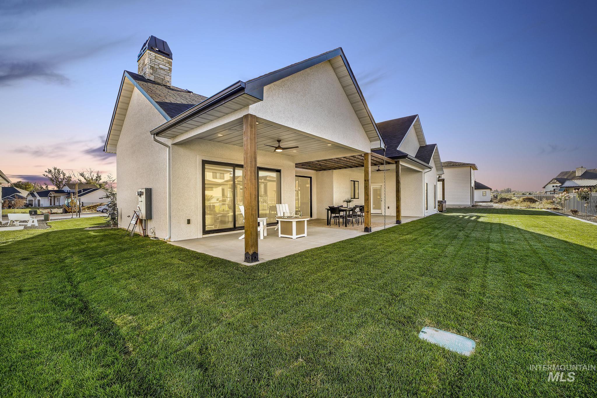 Back of house featuring a ceiling fan, stucco siding, a patio area, a yard, and a chimney