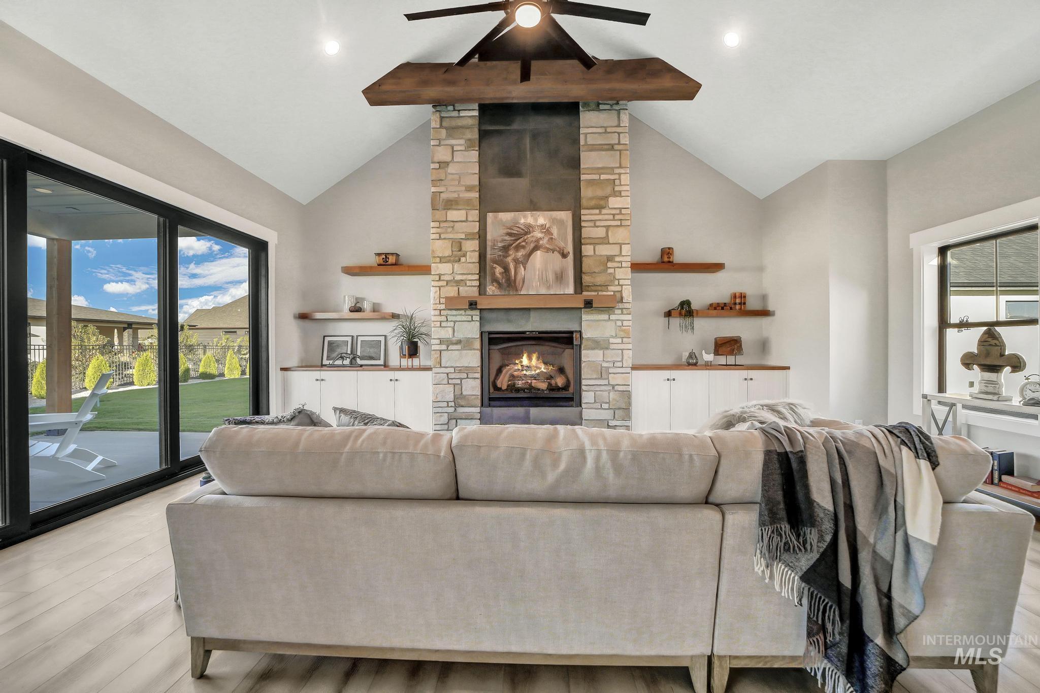 Living area with a stone fireplace, wood finished floors, beamed ceiling, ceiling fan, and high vaulted ceiling