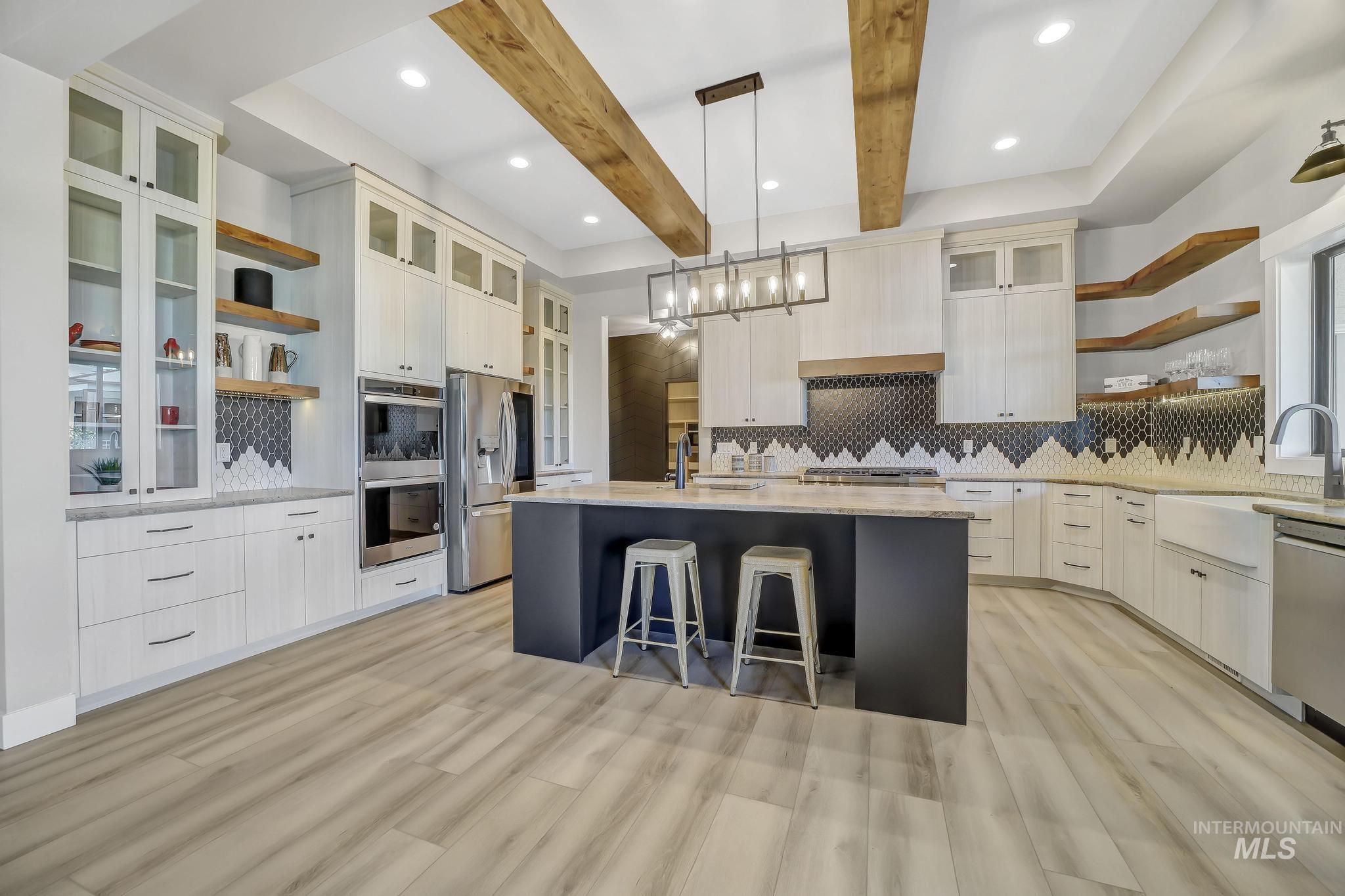 Kitchen featuring open shelves, decorative light fixtures, glass insert cabinets, appliances with stainless steel finishes, and beamed ceiling