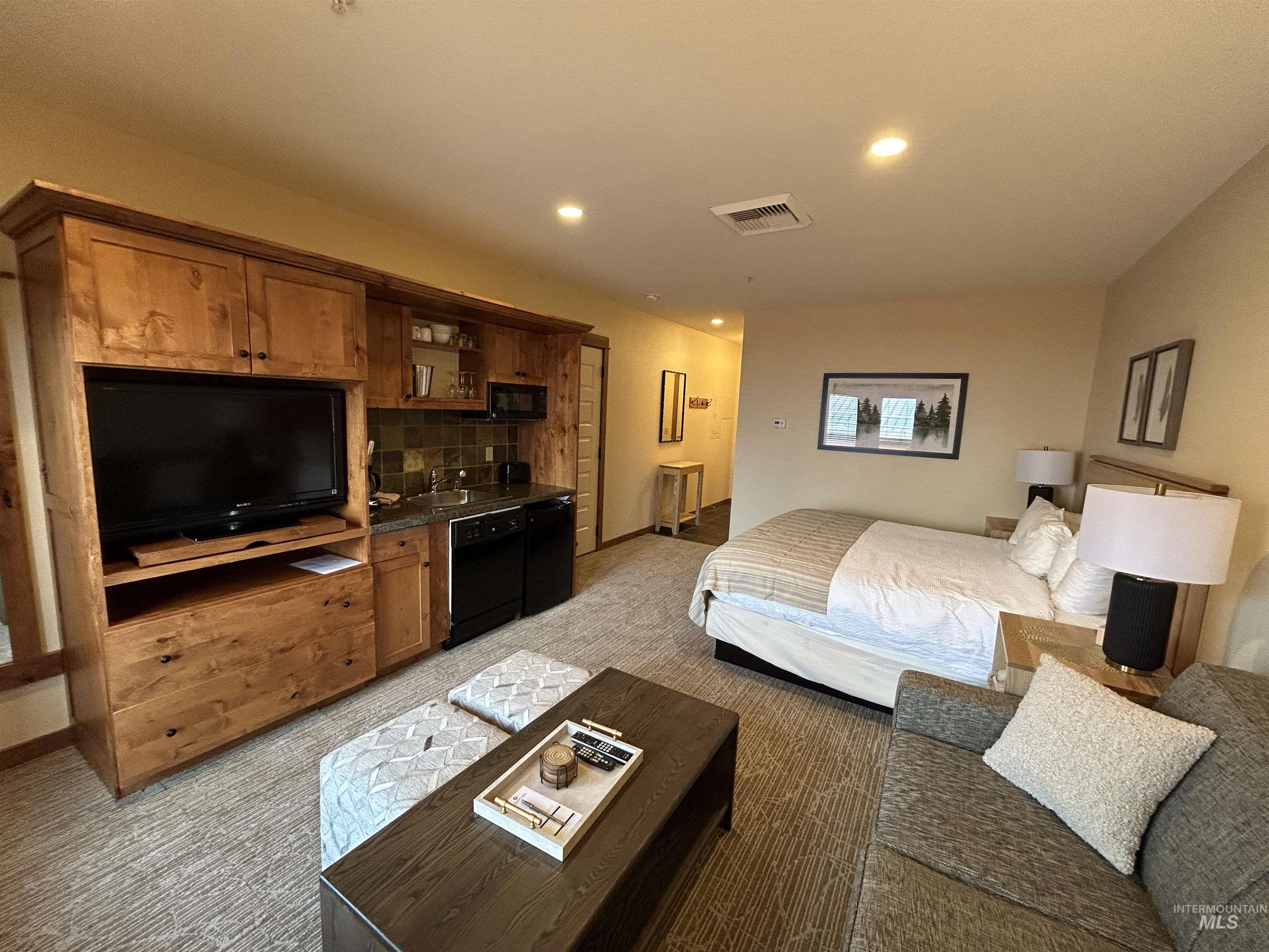Bedroom with light colored carpet, recessed lighting, and black refrigerator