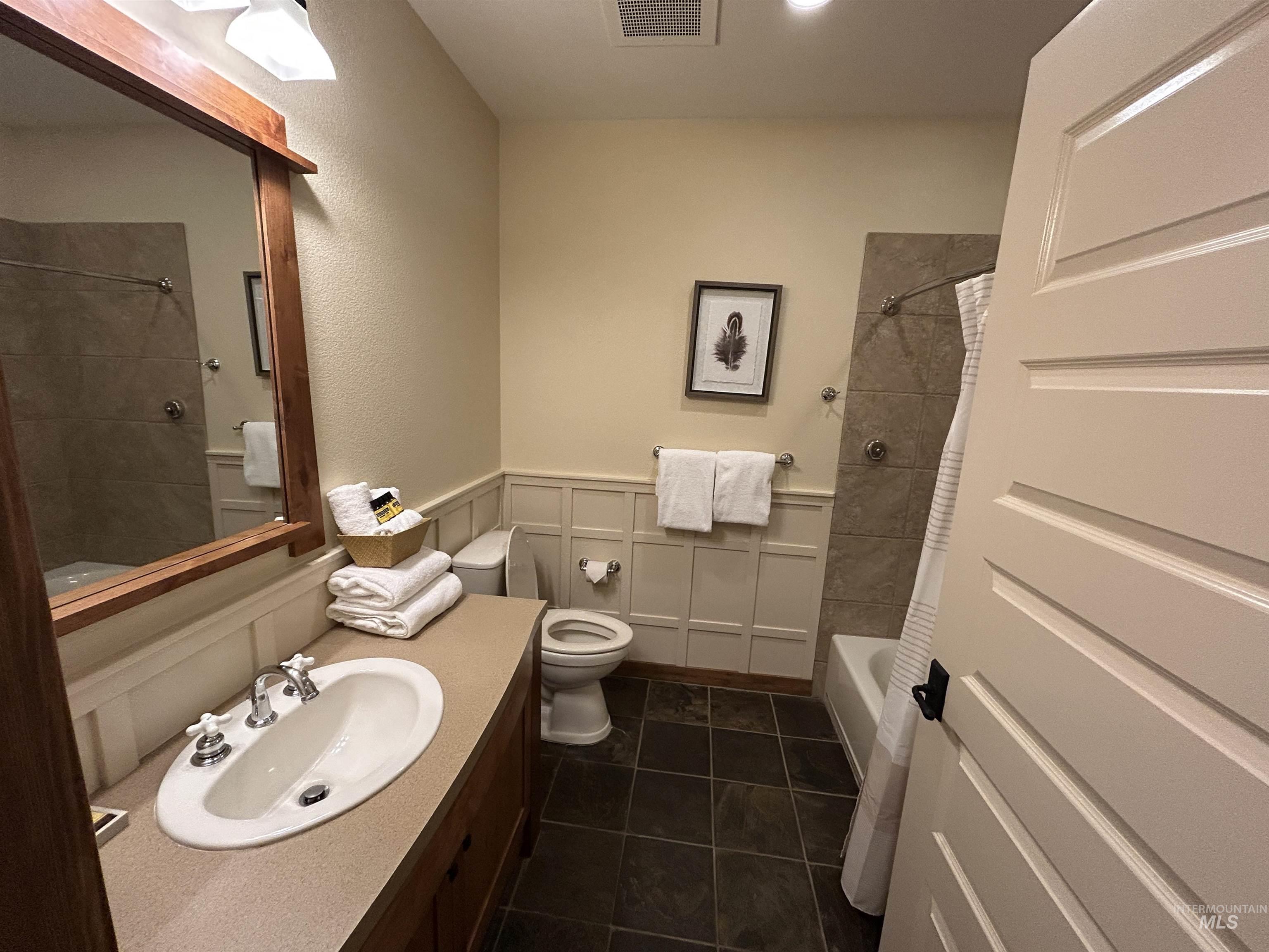 Bathroom featuring shower / bath combo, vanity, dark tile patterned flooring, wainscoting, and a decorative wall