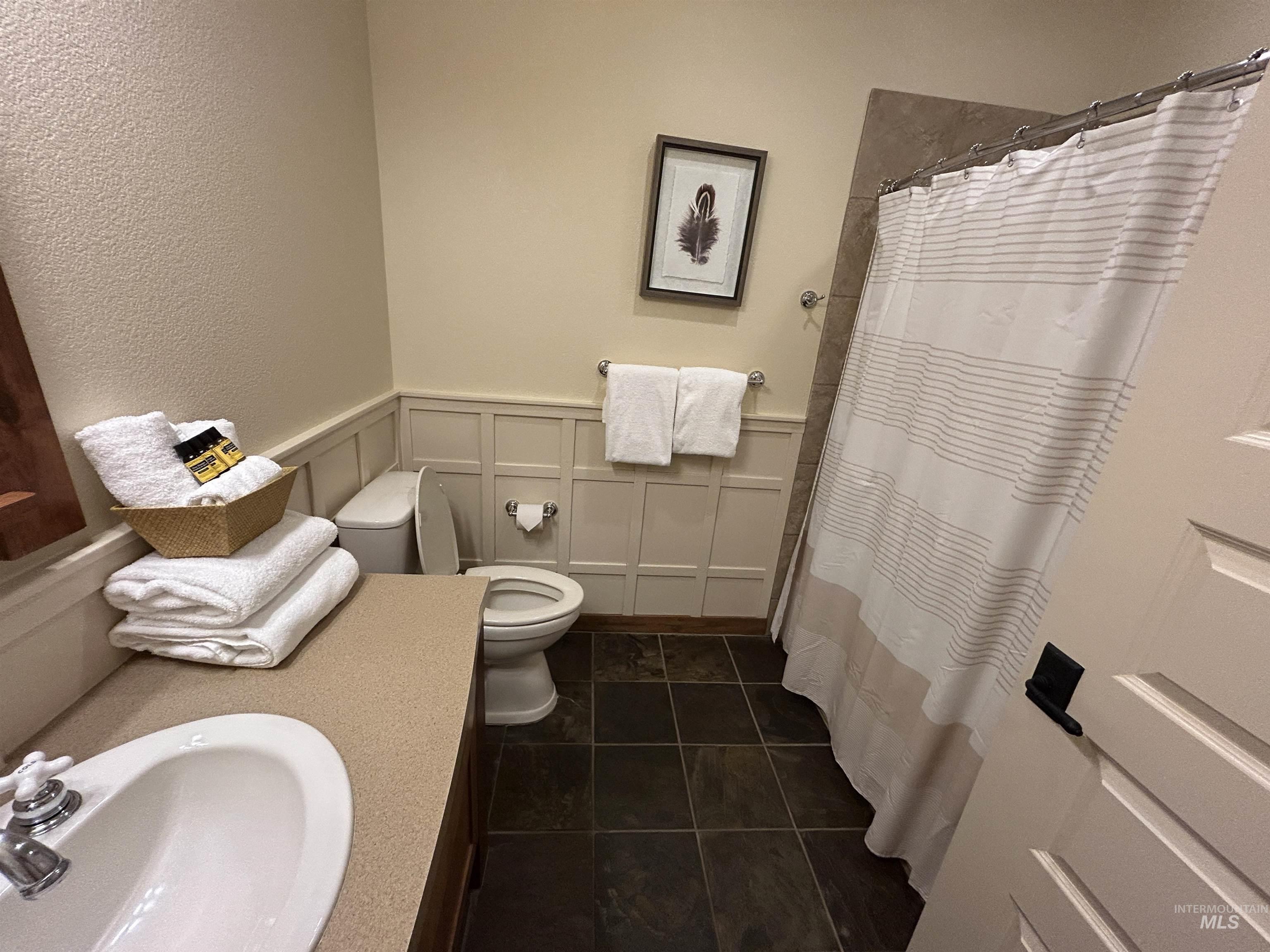 Full bathroom featuring a decorative wall, wainscoting, a textured wall, vanity, and a shower with curtain