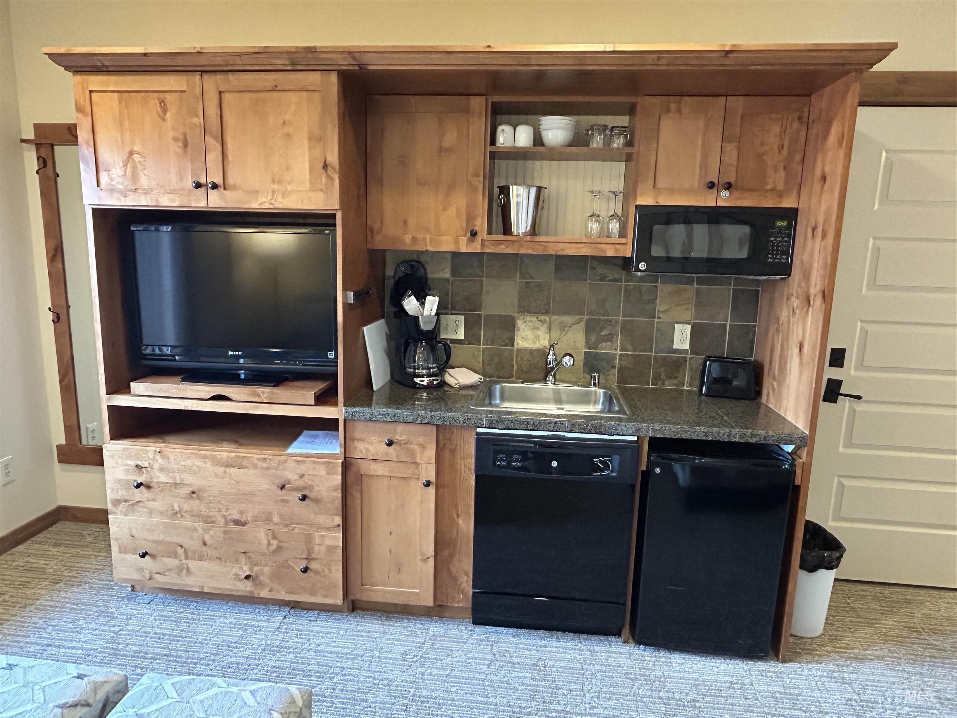 Kitchen featuring black appliances, decorative backsplash, dark countertops, and light carpet