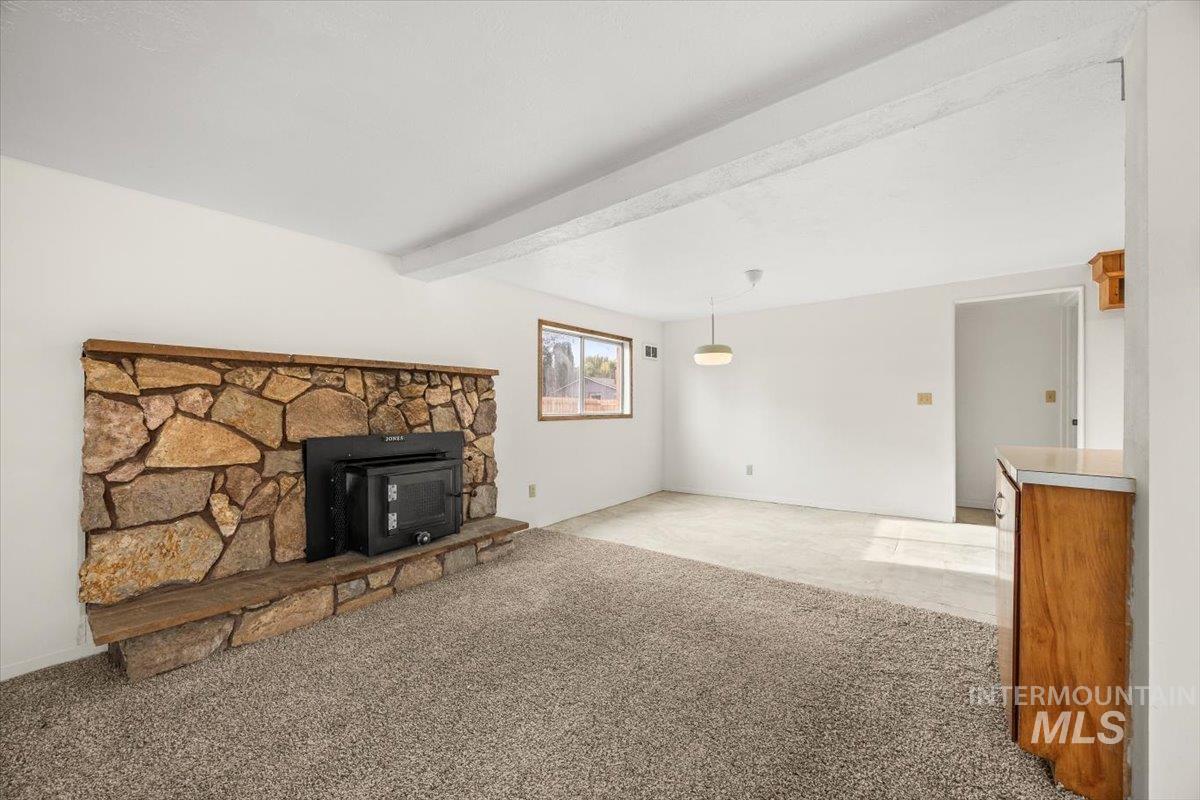 Unfurnished living room featuring light carpet, beam ceiling, and a fireplace