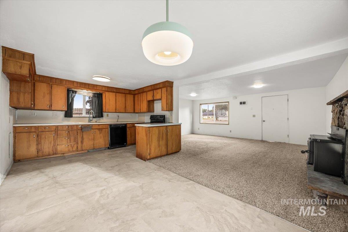 Kitchen featuring brown cabinets, light countertops, open floor plan, dishwasher, and light carpet