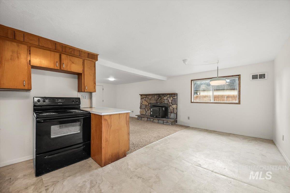 Kitchen featuring brown cabinetry, black range with electric stovetop, open floor plan, light countertops, and a wood stove