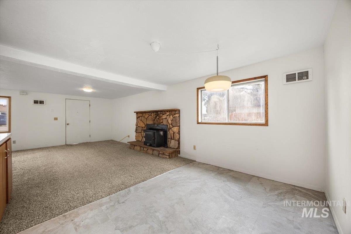 Unfurnished living room with beam ceiling, plenty of natural light, light carpet, and a wood stove