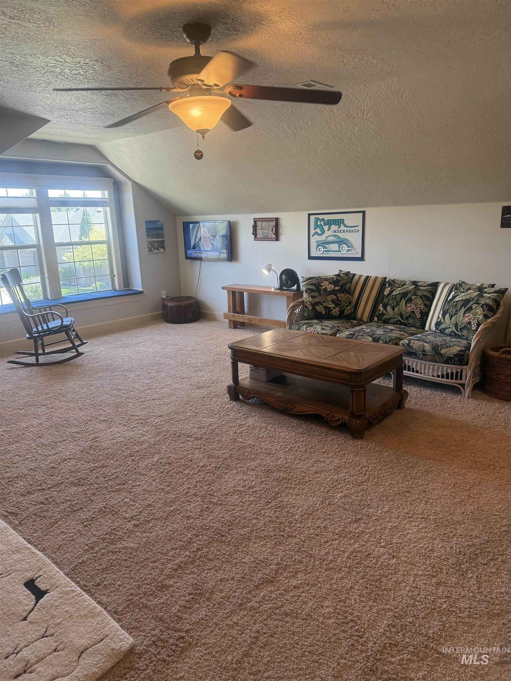 Living room featuring a textured ceiling, carpet floors, vaulted ceiling, and a ceiling fan