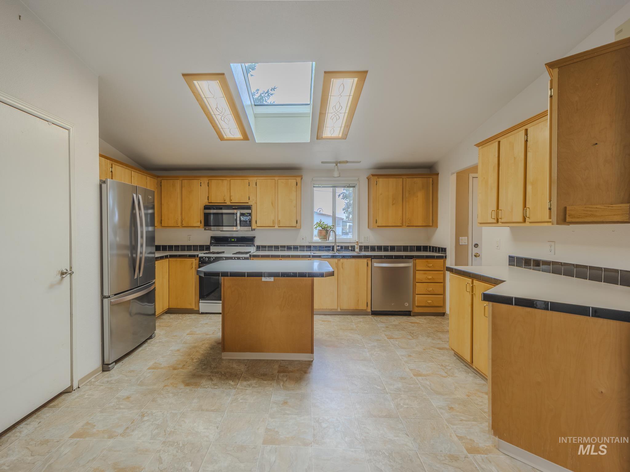 Kitchen with a skylight, appliances with stainless steel finishes, and a kitchen island