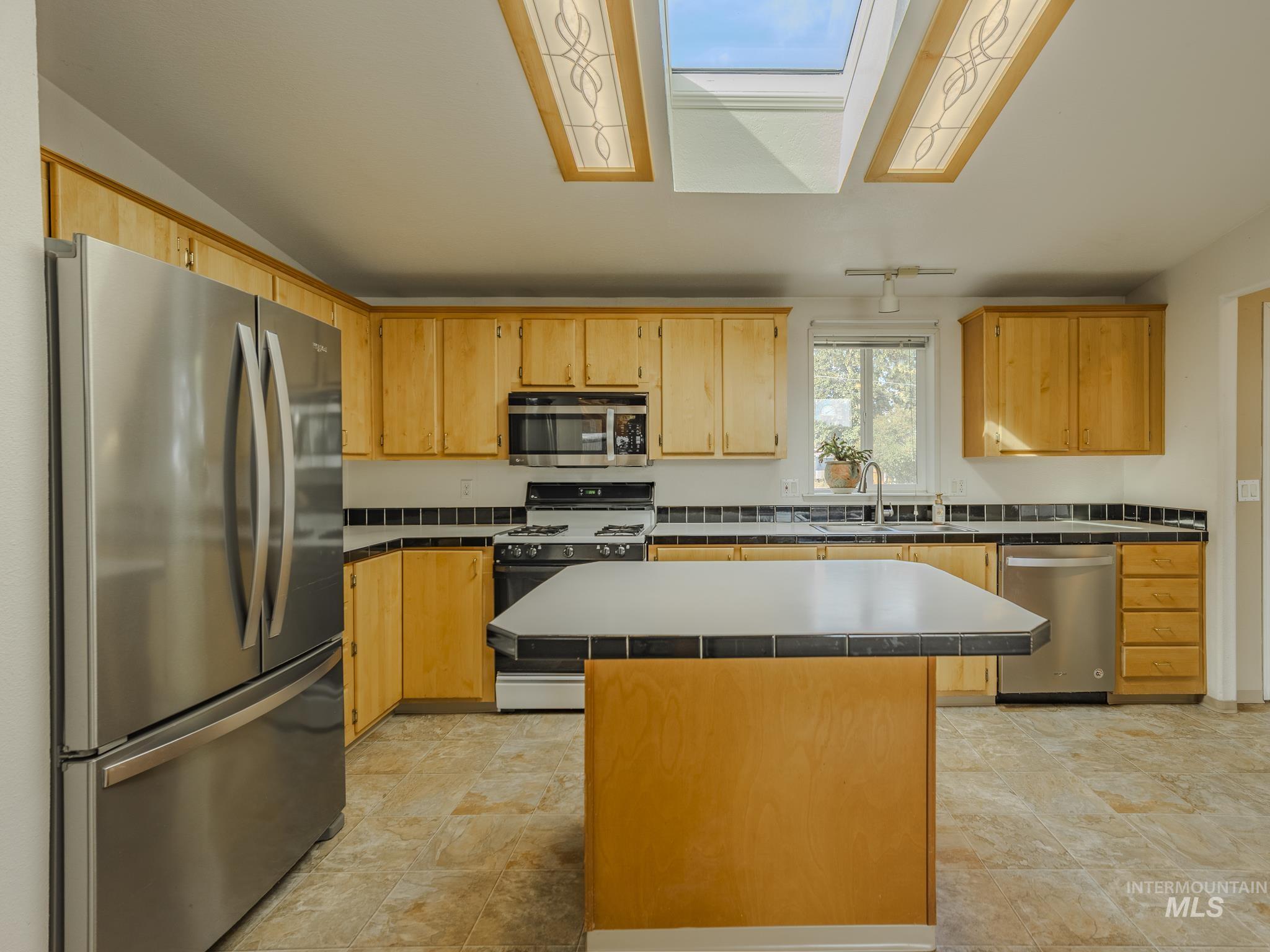 Kitchen featuring appliances with stainless steel finishes, a center island, and a skylight