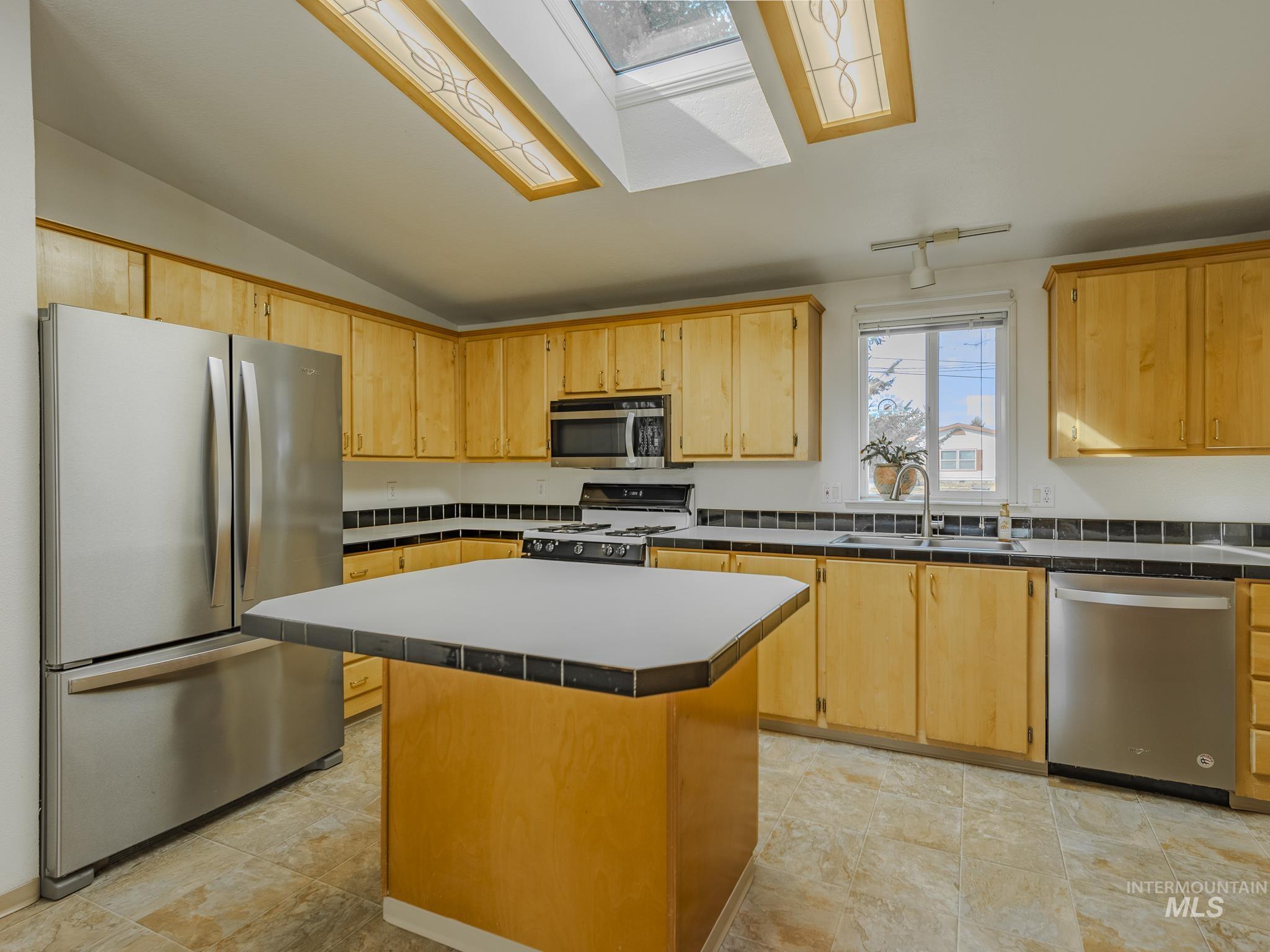 Kitchen with appliances with stainless steel finishes, a skylight, a center island, tile counters, and vaulted ceiling