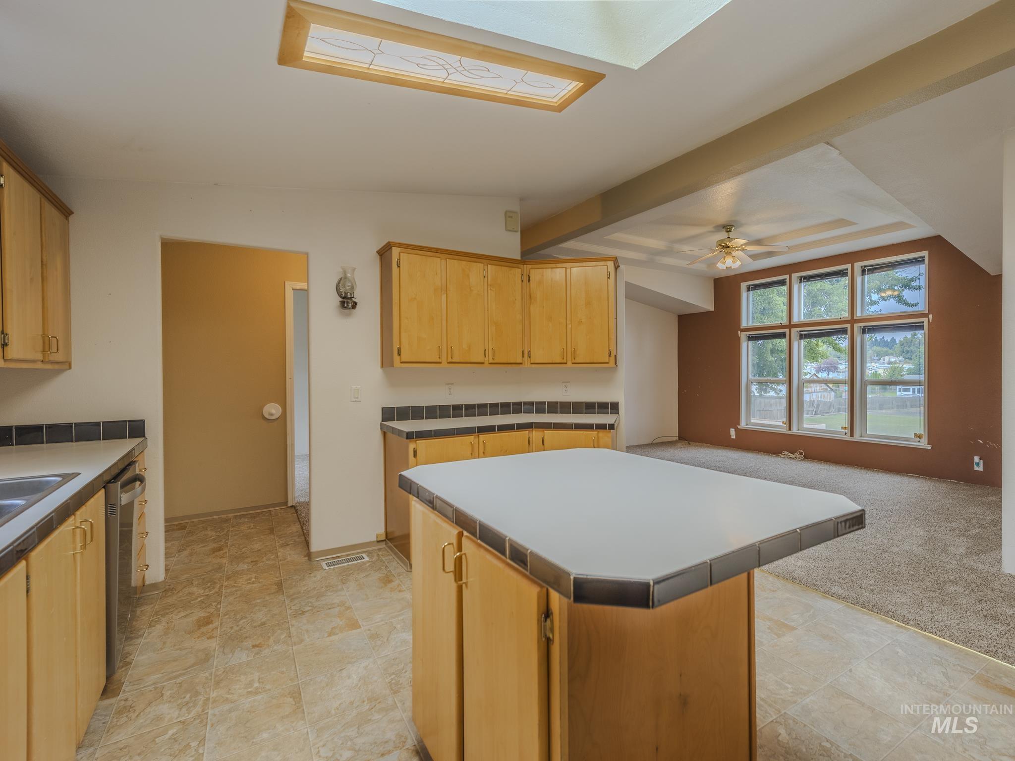 Kitchen with a center island, light brown cabinetry, open floor plan, stainless steel dishwasher, and a skylight