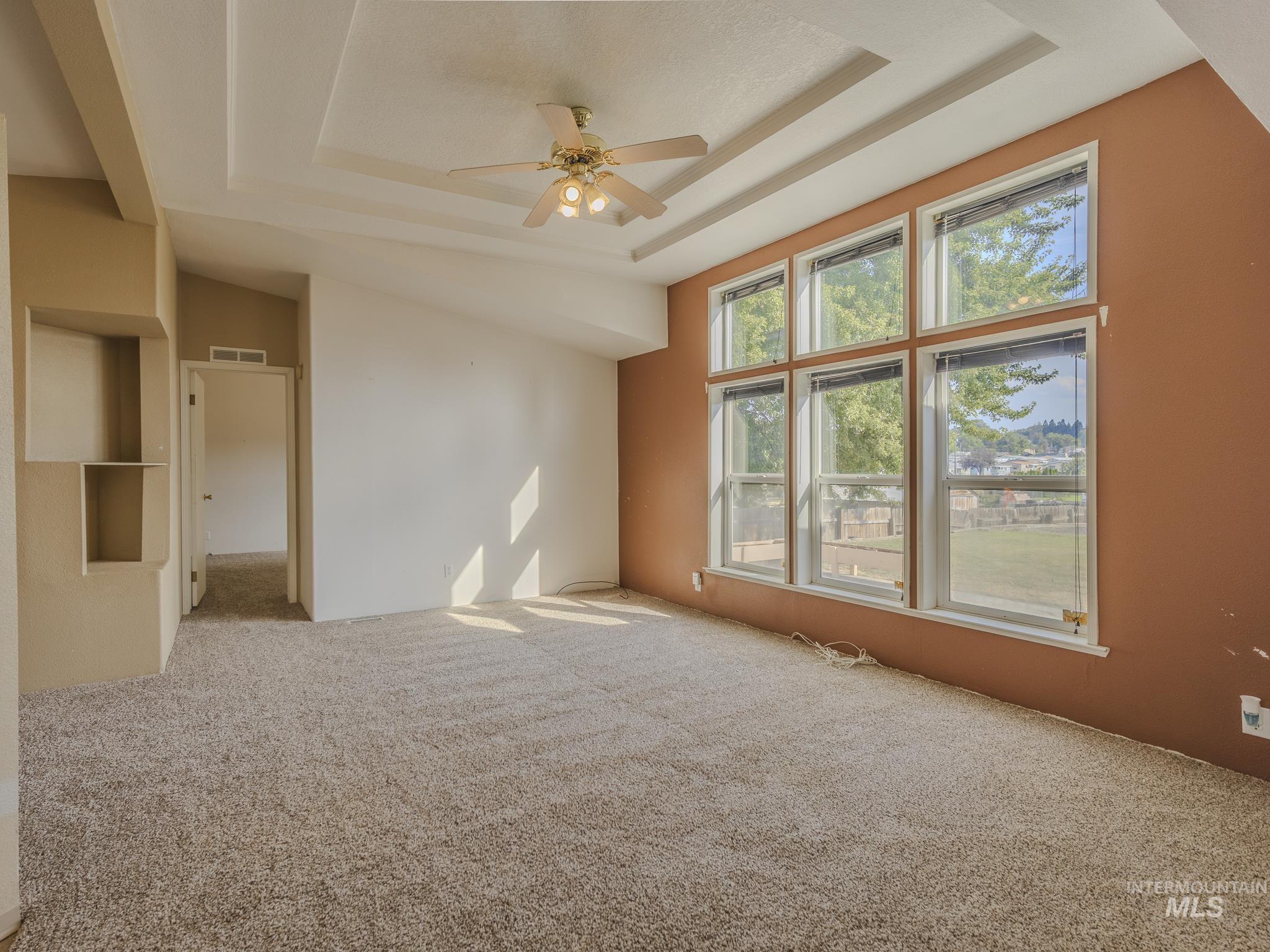 Empty room featuring carpet, a raised ceiling, and ceiling fan