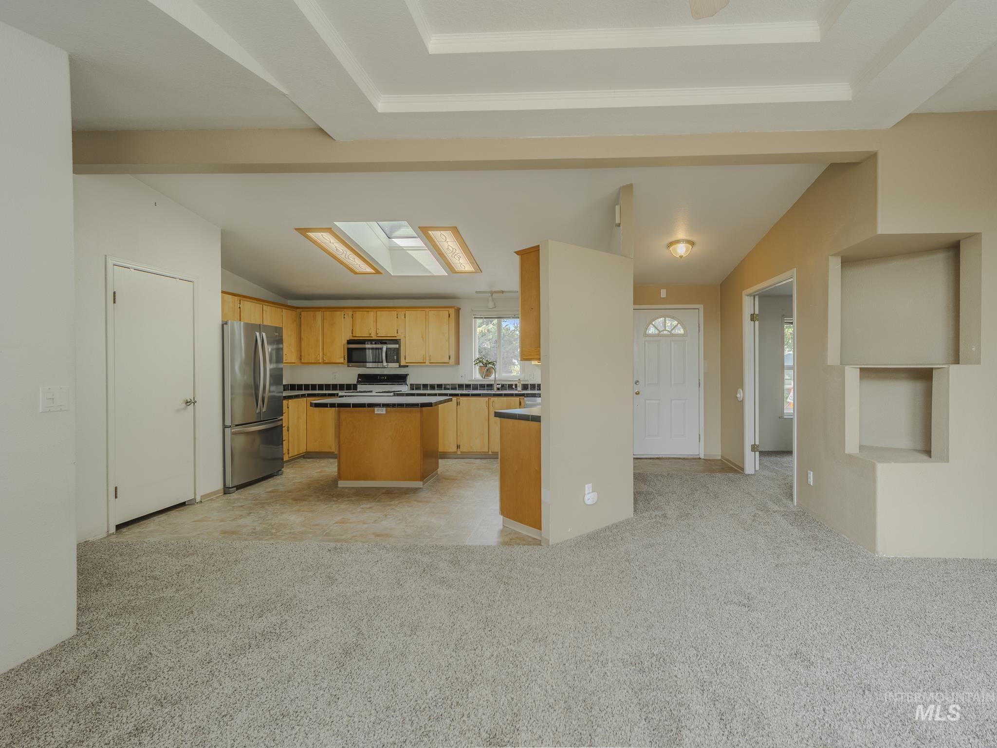 Kitchen with a center island, lofted ceiling, light carpet, stainless steel appliances, and dark countertops