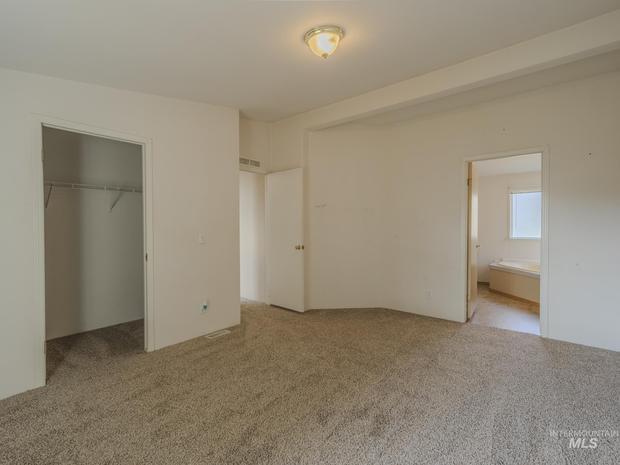 Unfurnished bedroom featuring carpet flooring, a spacious closet, and ensuite bath