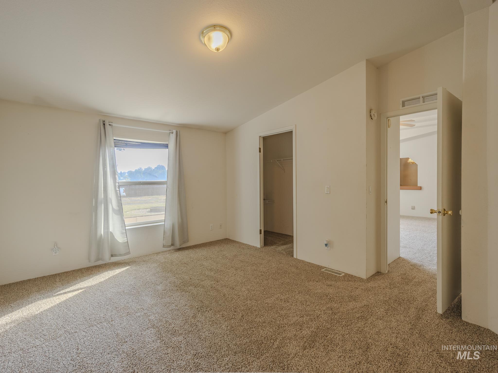 Unfurnished bedroom featuring a walk in closet, carpet floors, and lofted ceiling