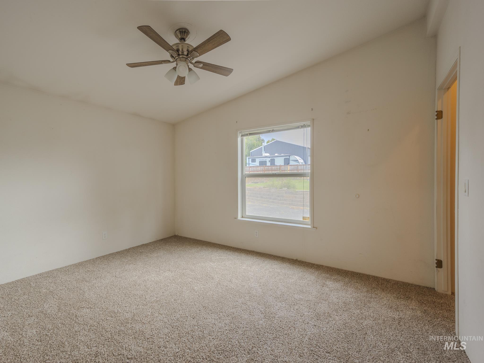 Carpeted empty room featuring vaulted ceiling and ceiling fan