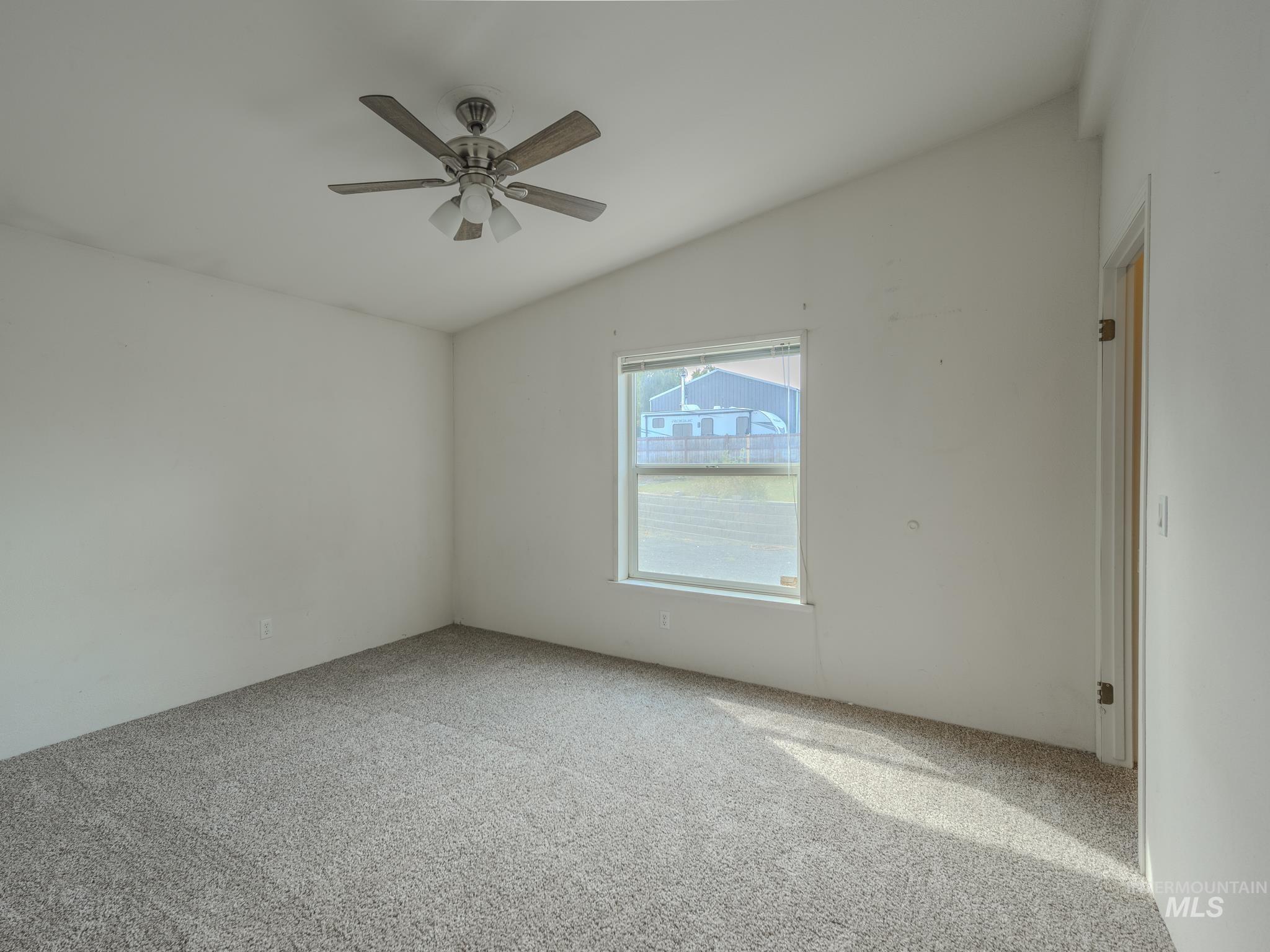 Carpeted empty room featuring lofted ceiling and a ceiling fan