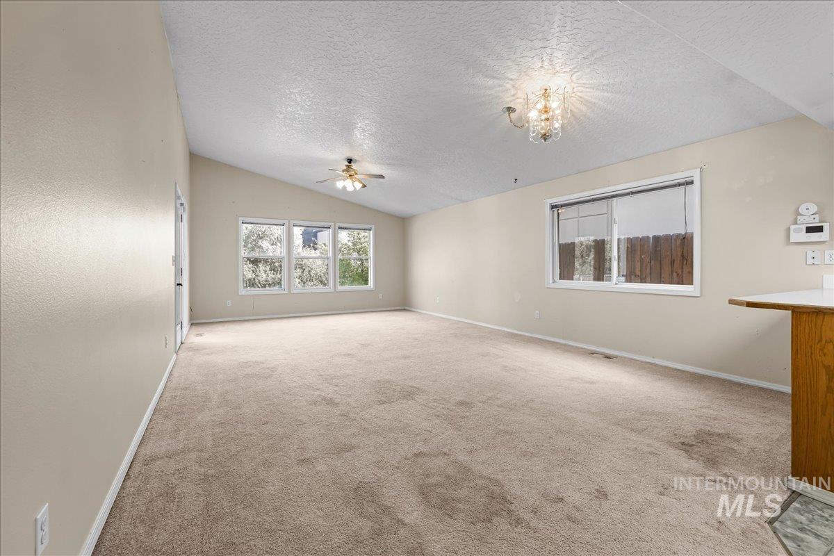 Unfurnished living room featuring a textured ceiling, carpet flooring, and vaulted ceiling