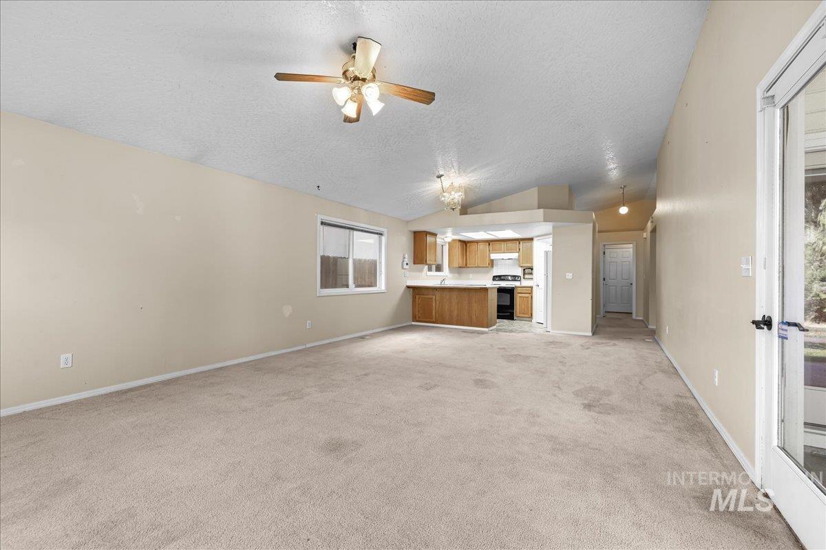 Unfurnished living room featuring a textured ceiling, light carpet, ceiling fan, and lofted ceiling