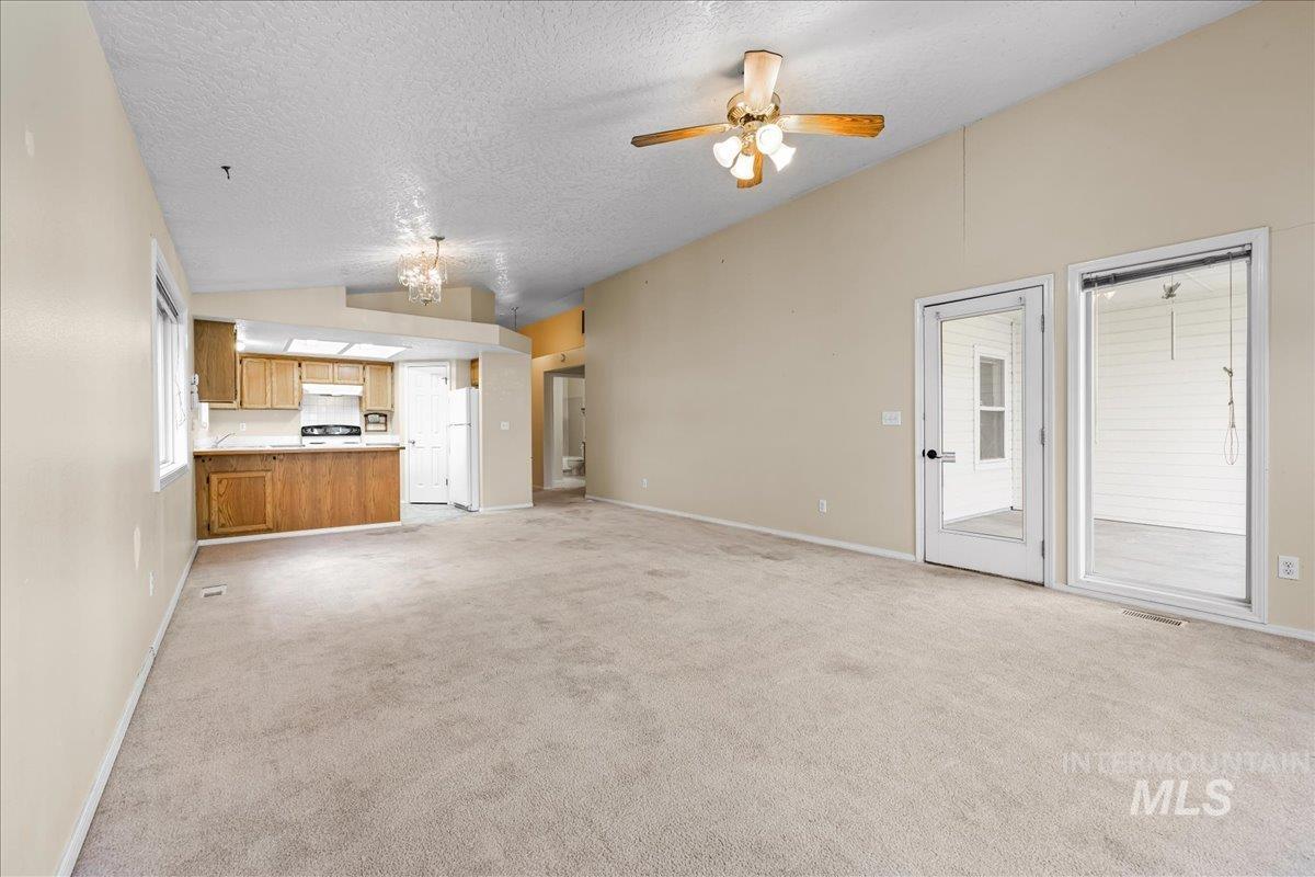 Unfurnished living room featuring a textured ceiling, light carpet, vaulted ceiling, and ceiling fan