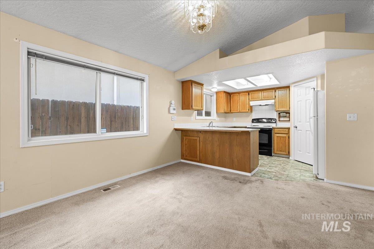 Kitchen with a textured ceiling, light carpet, light countertops, range with electric stovetop, and vaulted ceiling