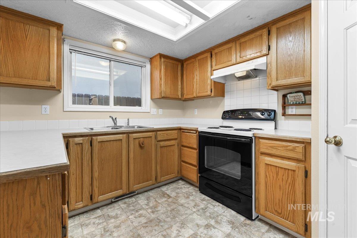 Kitchen with light countertops, black electric range, brown cabinetry, under cabinet range hood, and decorative backsplash