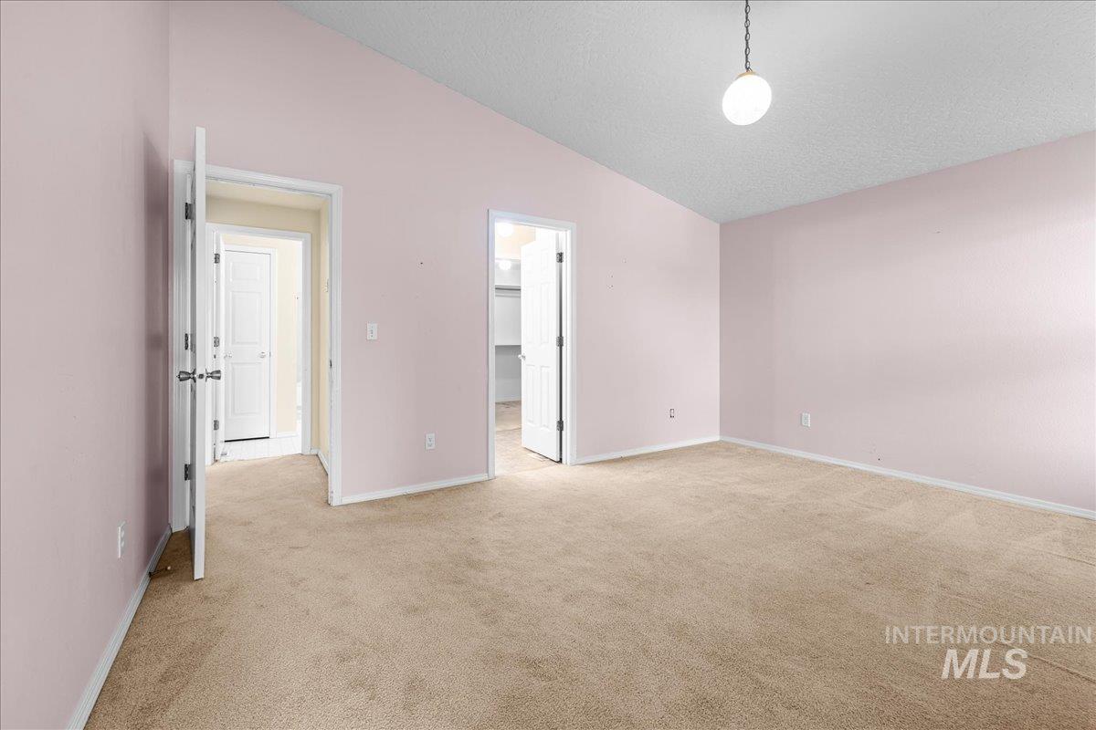Unfurnished bedroom featuring lofted ceiling, a walk in closet, light colored carpet, and a textured ceiling