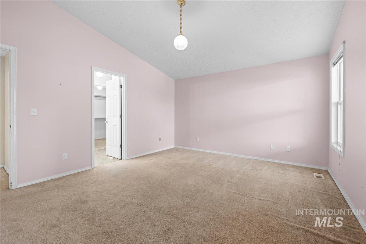 Unfurnished bedroom with a spacious closet, vaulted ceiling, light carpet, and a textured ceiling