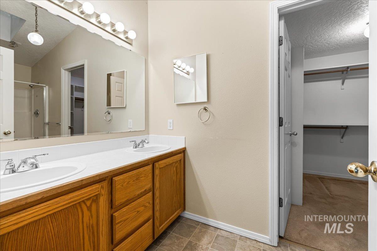 Bathroom featuring a textured ceiling, a spacious closet, a stall shower, double vanity, and light tile patterned floors
