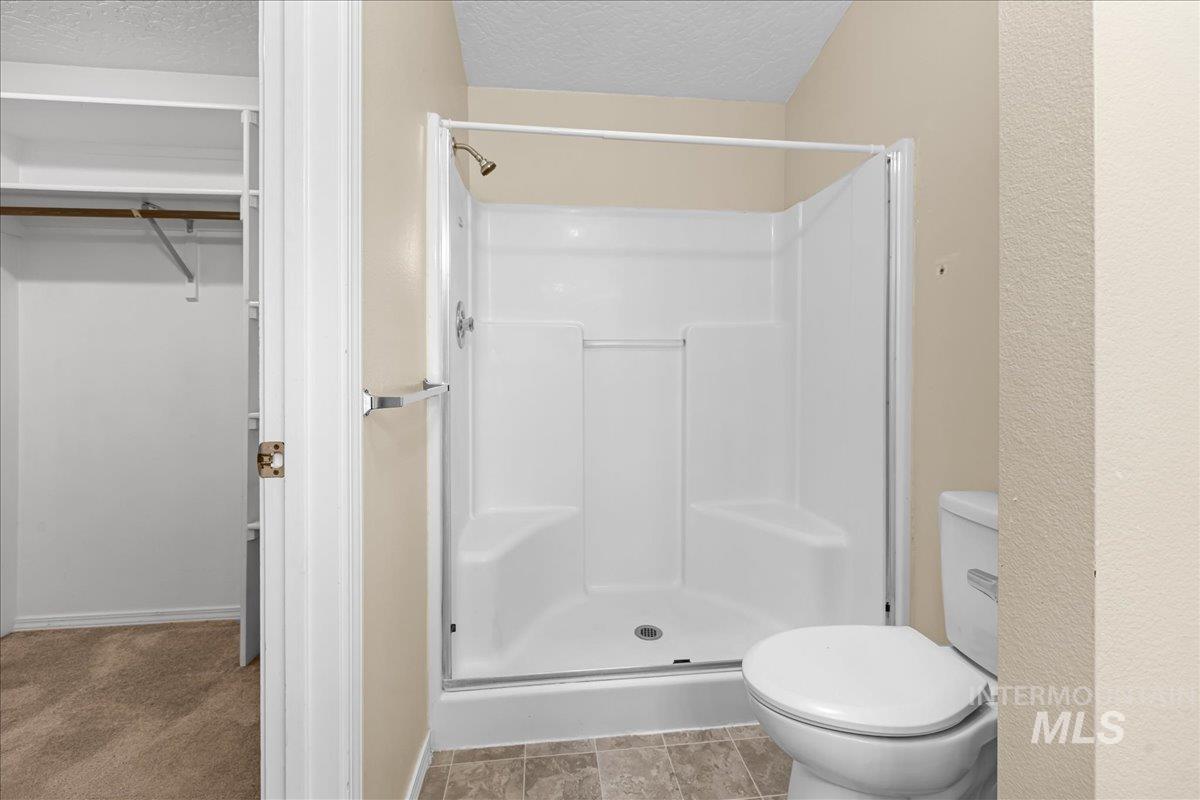 Full bathroom featuring a shower stall, a textured ceiling, and a closet