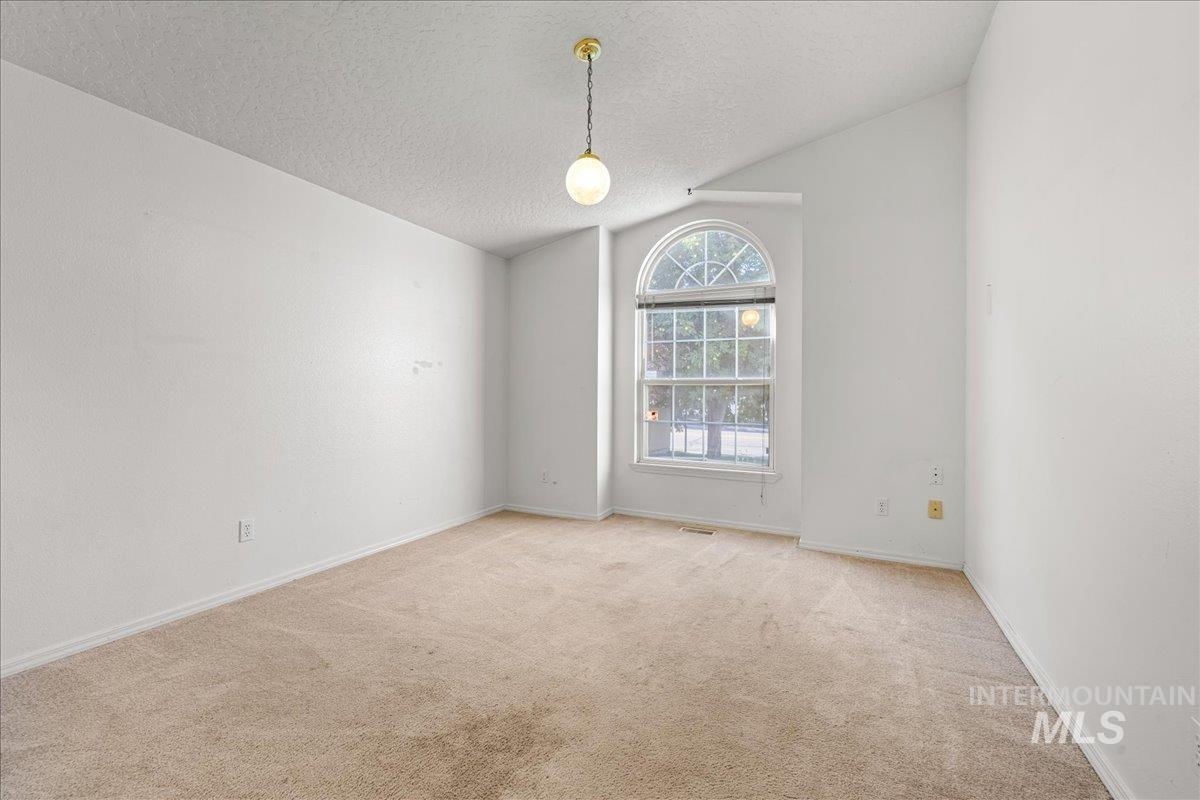 Carpeted spare room with a textured ceiling and vaulted ceiling