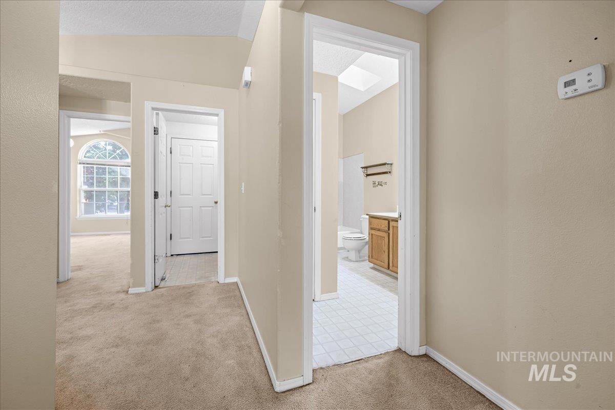 Corridor featuring light colored carpet, a textured ceiling, and vaulted ceiling
