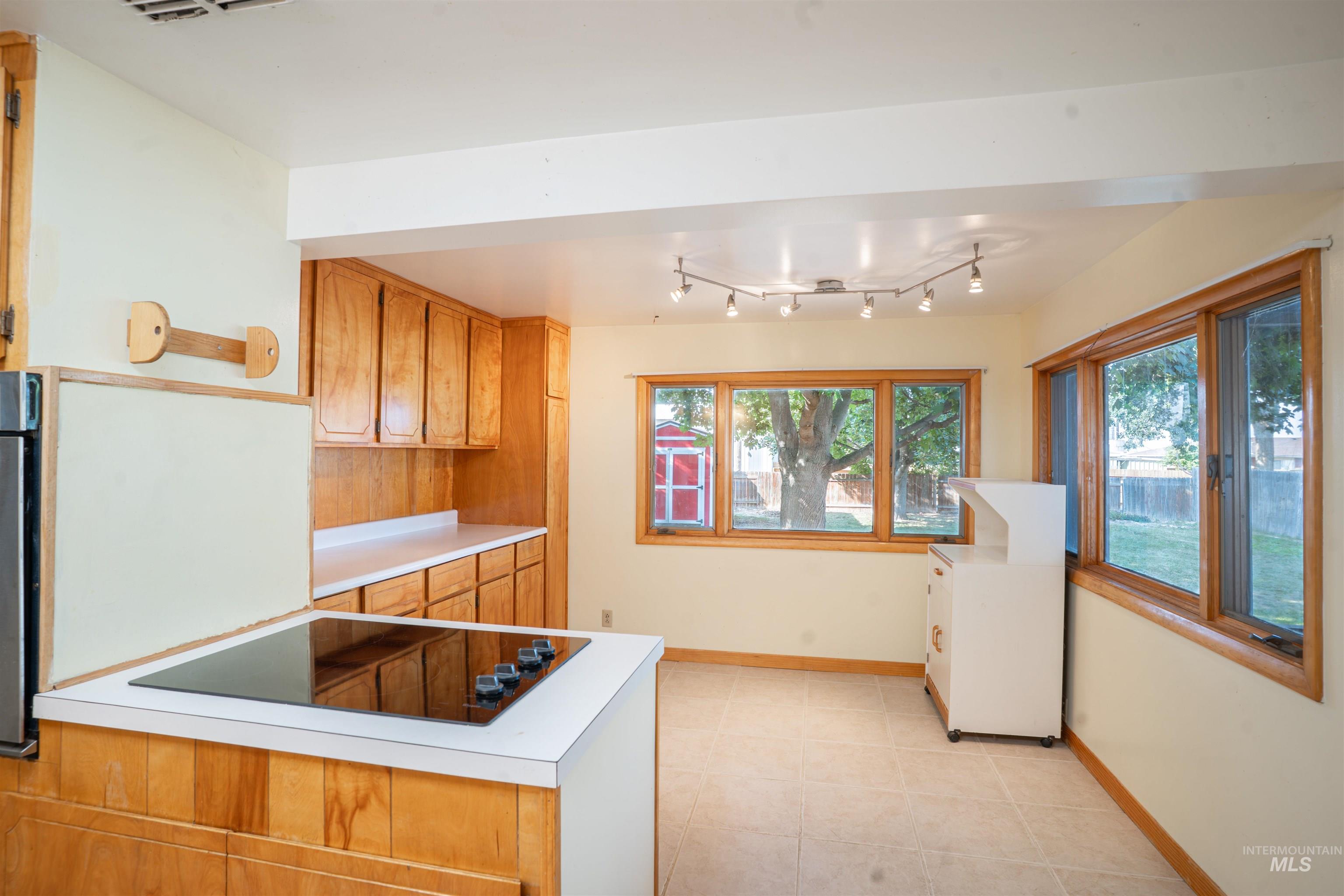 Kitchen featuring brown cabinets, light countertops, black appliances, light tile patterned flooring, and a peninsula