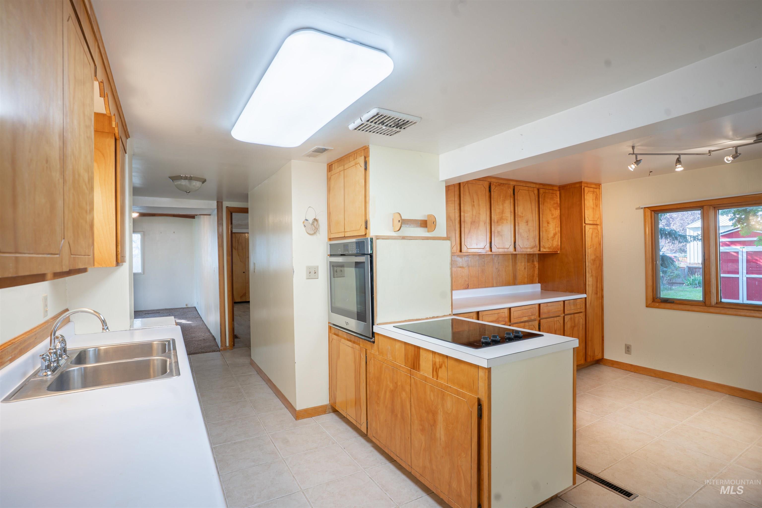 Kitchen featuring a peninsula, light countertops, oven, black electric cooktop, and light tile patterned floors