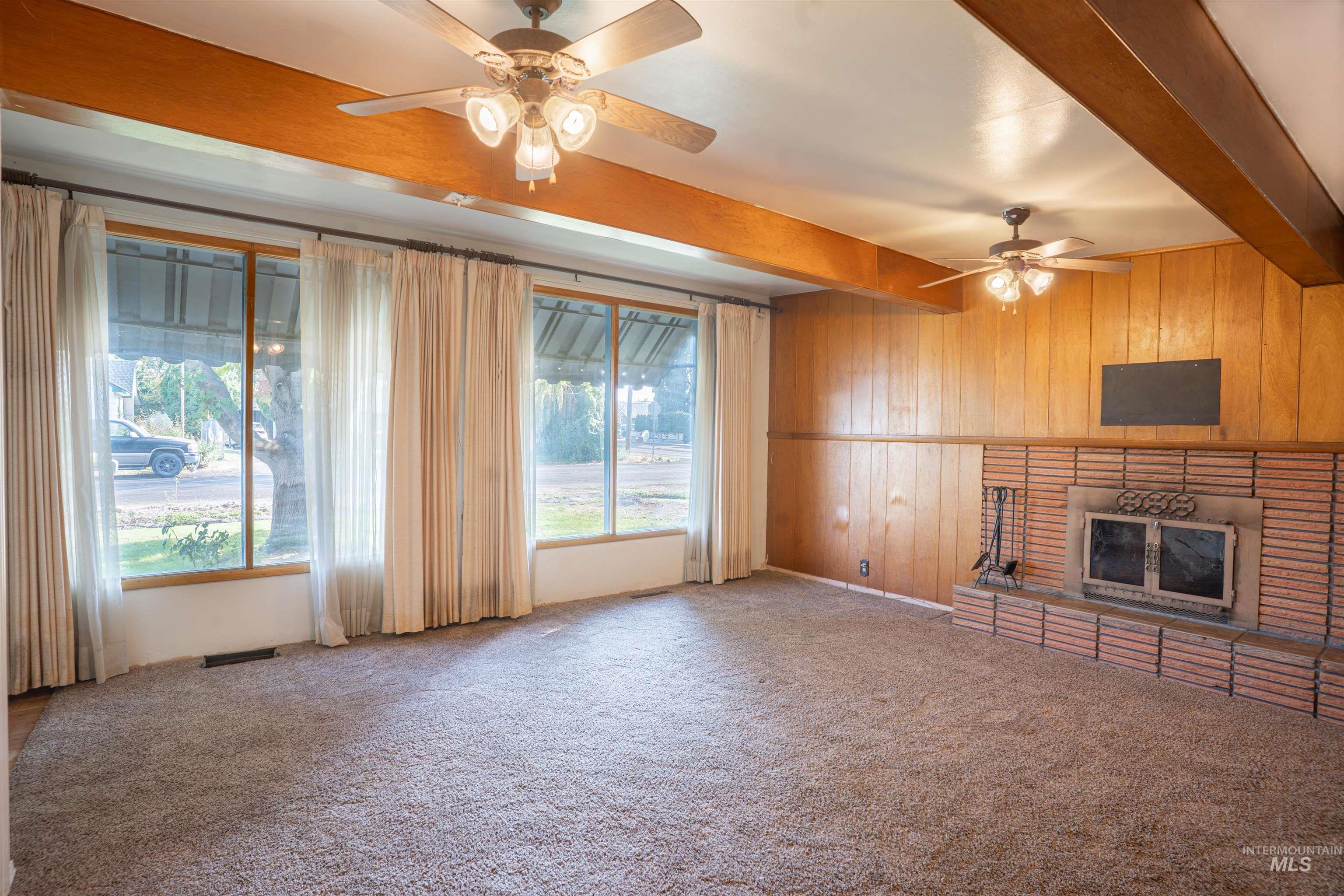 Unfurnished living room featuring beam ceiling, wooden walls, a ceiling fan, carpet floors, and a fireplace
