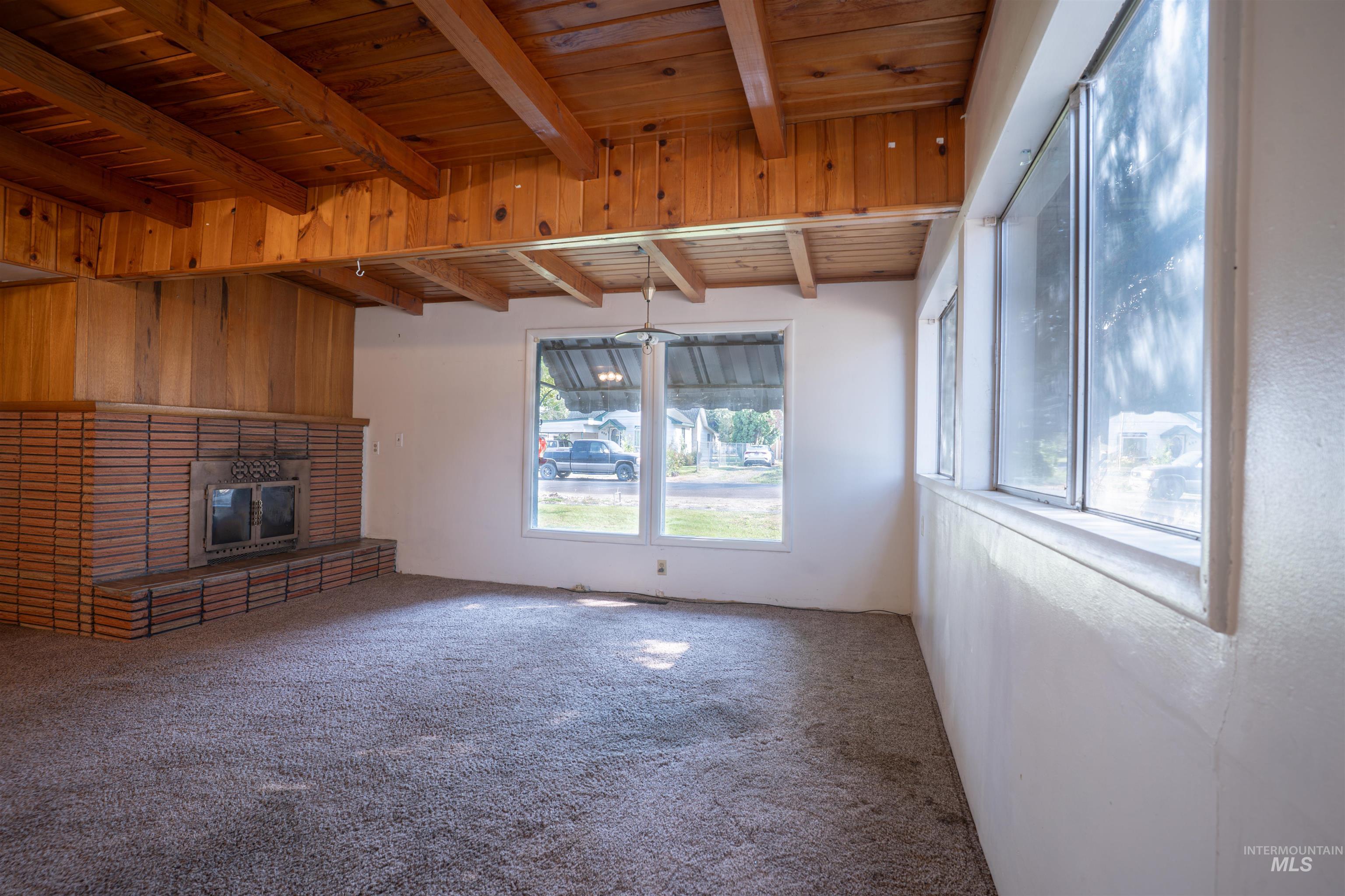 Unfurnished living room with a wooden ceiling with exposed beams, carpet flooring, a fireplace, and wooden walls