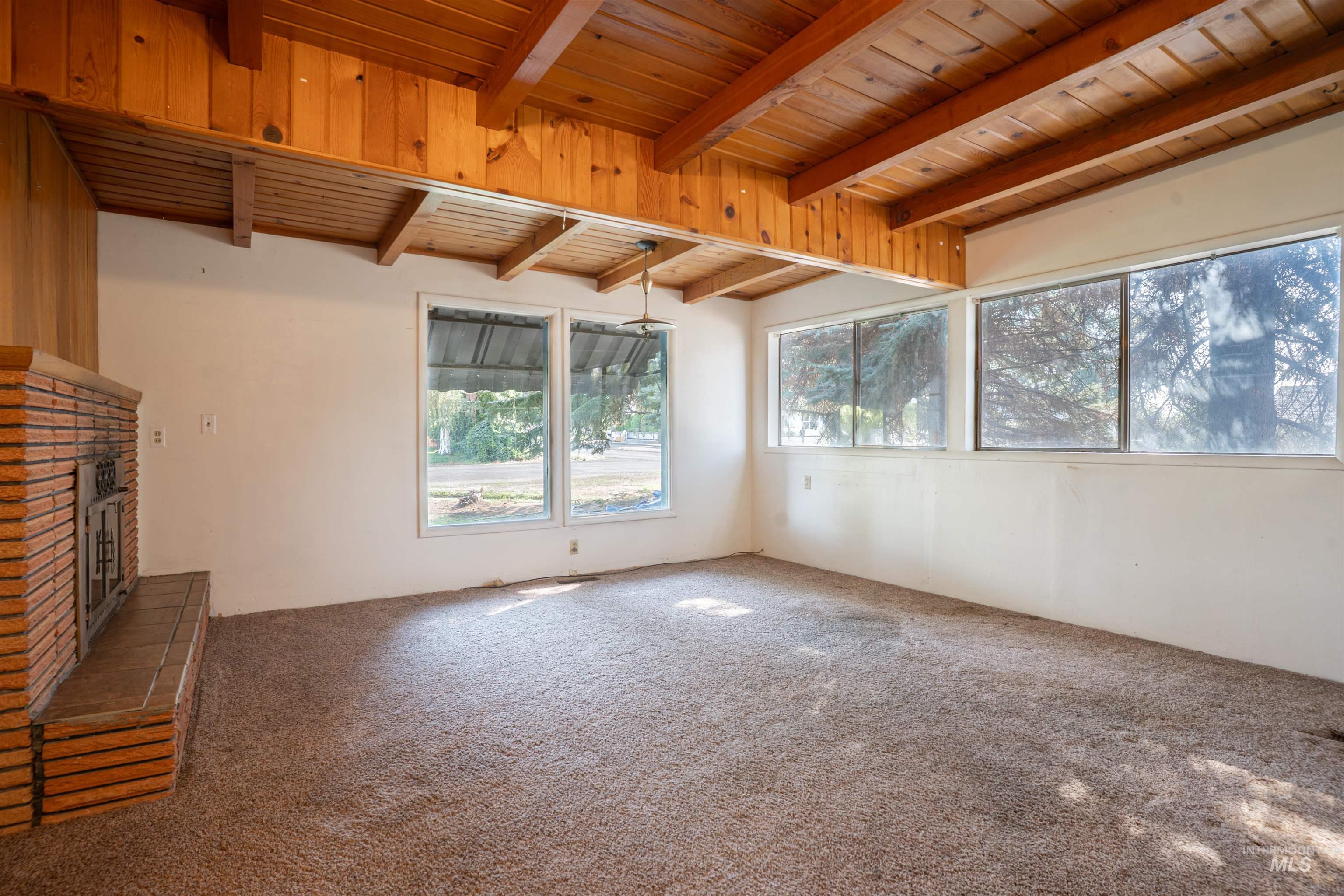 Unfurnished living room featuring a fireplace, healthy amount of natural light, a wood ceiling with exposed beams, and carpet