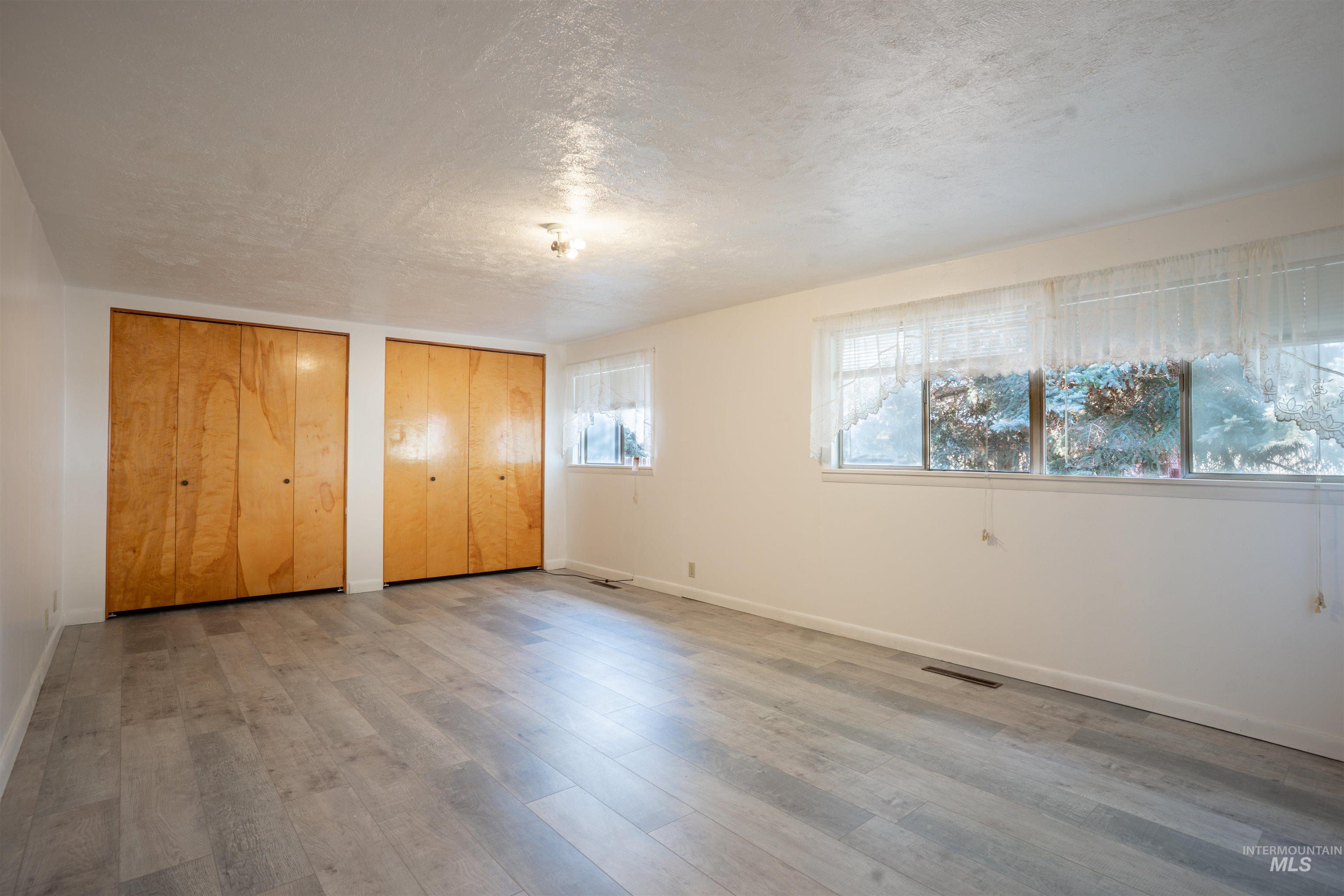 Unfurnished bedroom with multiple closets, a textured ceiling, and wood finished floors