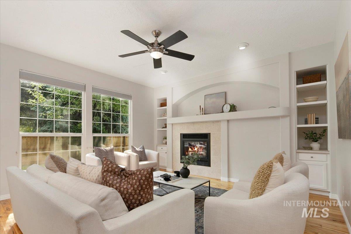 Living room featuring light wood-style flooring, built in shelves, a tile fireplace, a ceiling fan, and a textured ceiling