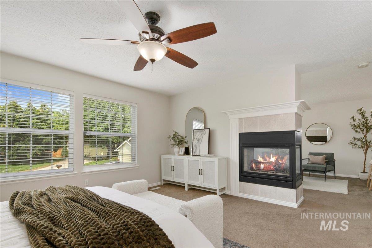 Carpeted bedroom featuring a tiled fireplace, a textured ceiling, and a ceiling fan