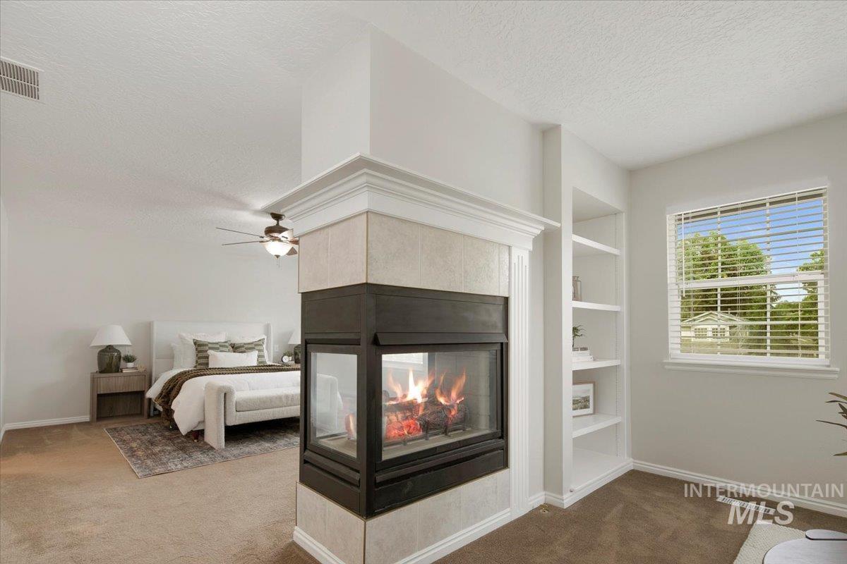 Carpeted bedroom with a textured ceiling, a multi sided fireplace, and a ceiling fan