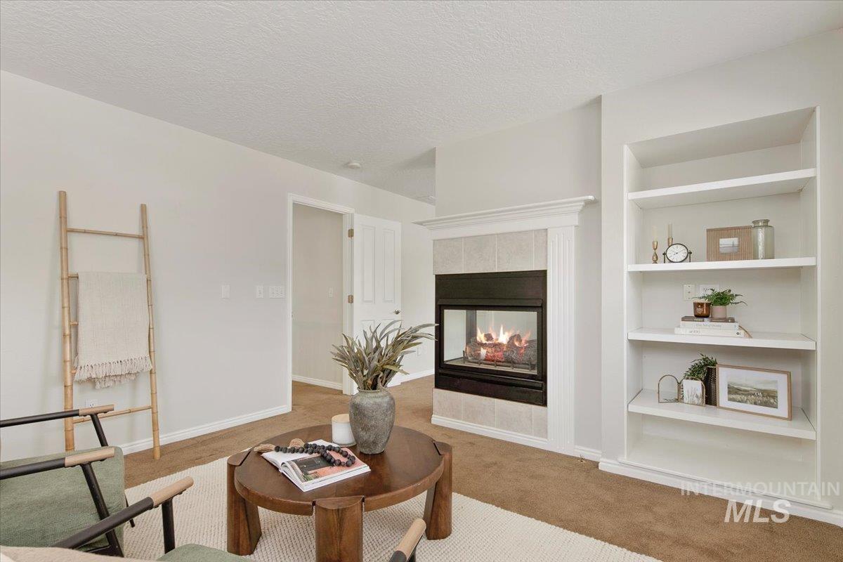 Living area with built in features, a tiled fireplace, carpet floors, and a textured ceiling