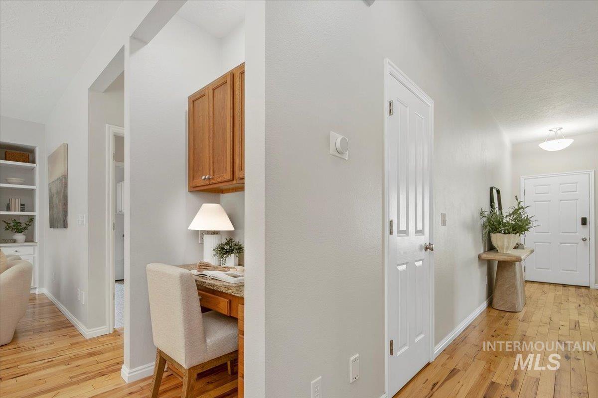 Hall with light wood-style flooring, a textured ceiling, and built in shelves