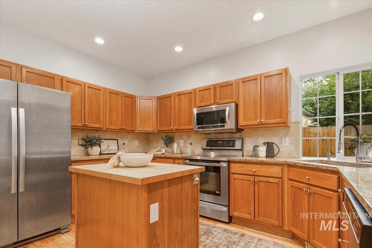 Kitchen featuring appliances with stainless steel finishes, butcher block countertops, tasteful backsplash, brown cabinetry, and recessed lighting