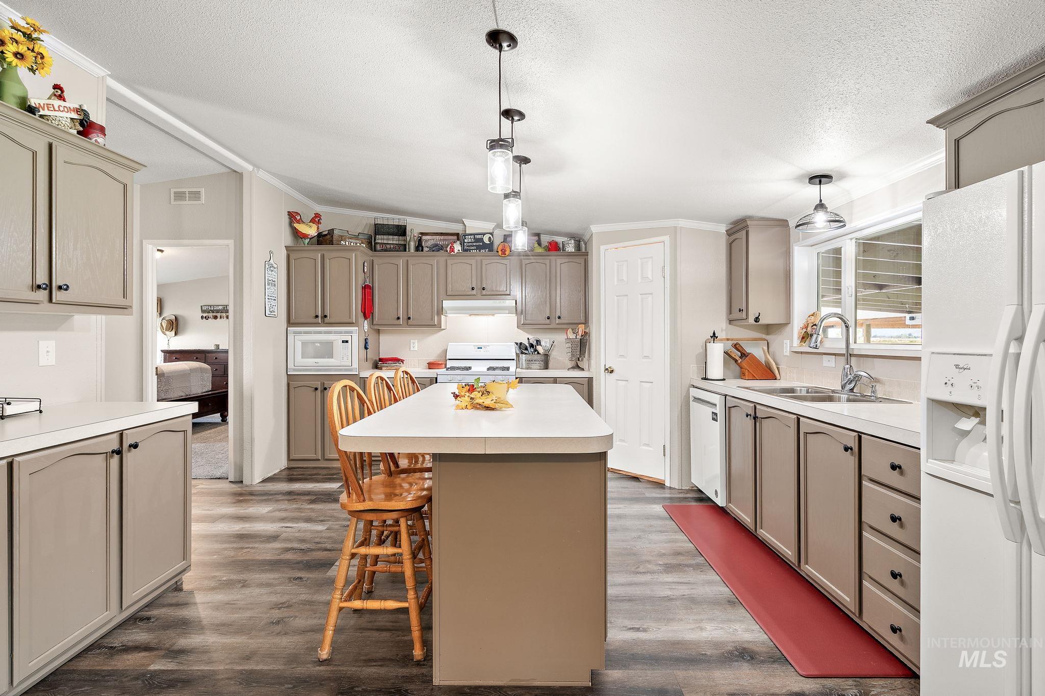 Kitchen with hanging light fixtures, a kitchen bar, white appliances, light countertops, and crown molding