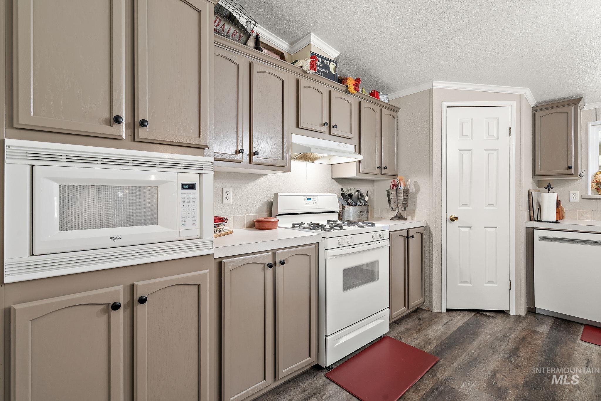 Kitchen featuring white appliances, dark wood-style flooring, light countertops, under cabinet range hood, and ornamental molding