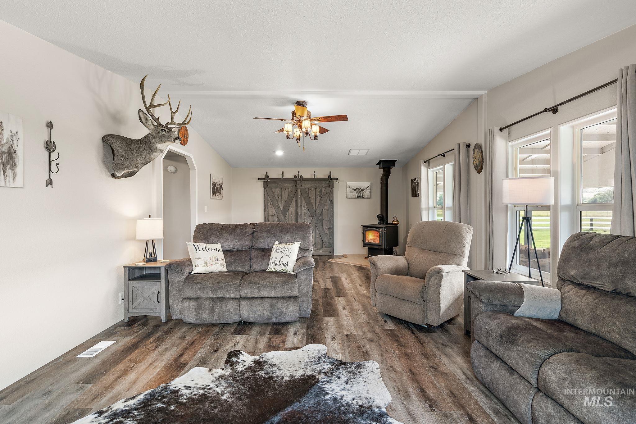 Living area with a wood stove, wood finished floors, ceiling fan, and a barn door