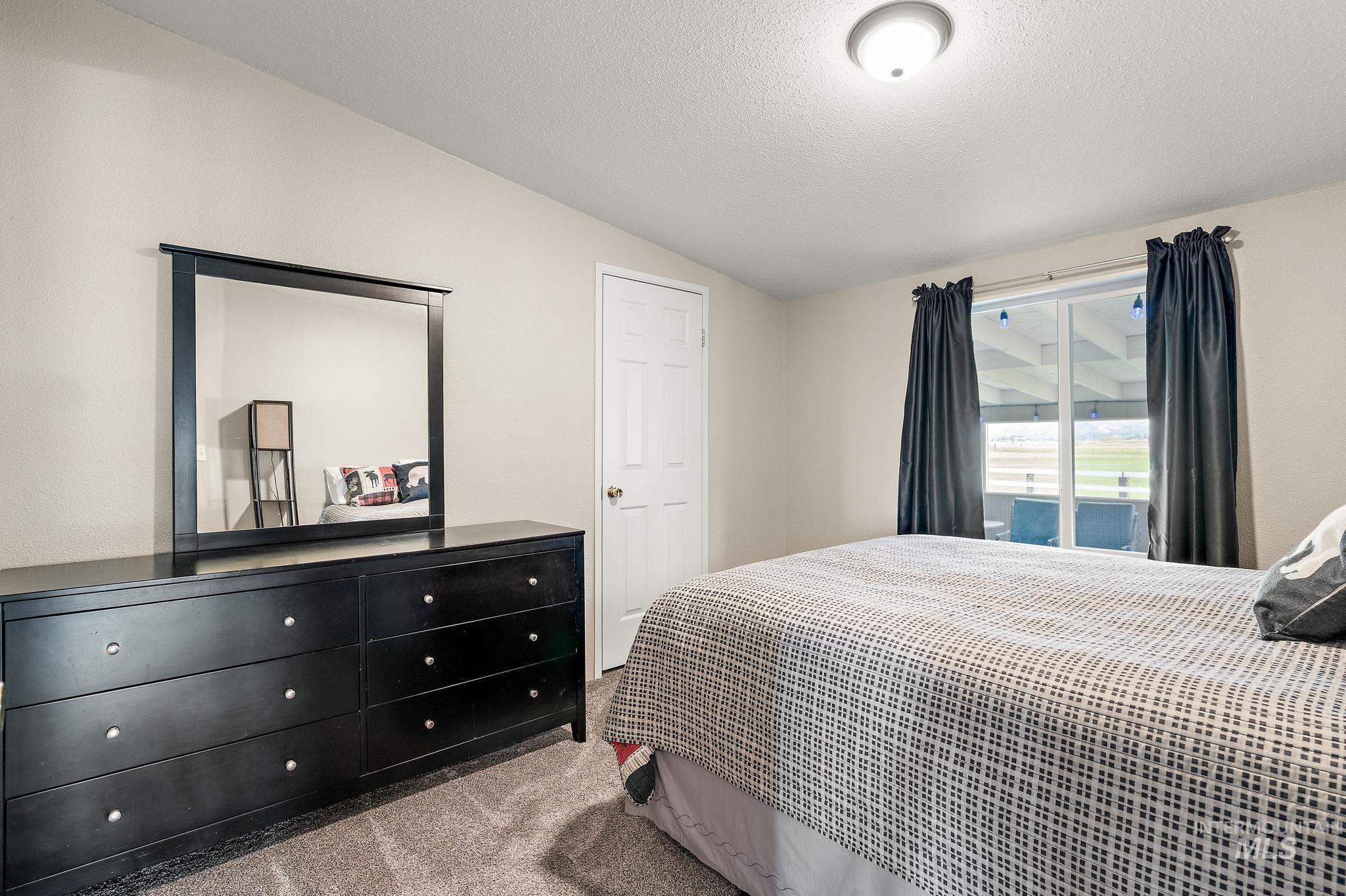 Carpeted bedroom featuring vaulted ceiling, a textured ceiling, and access to outside